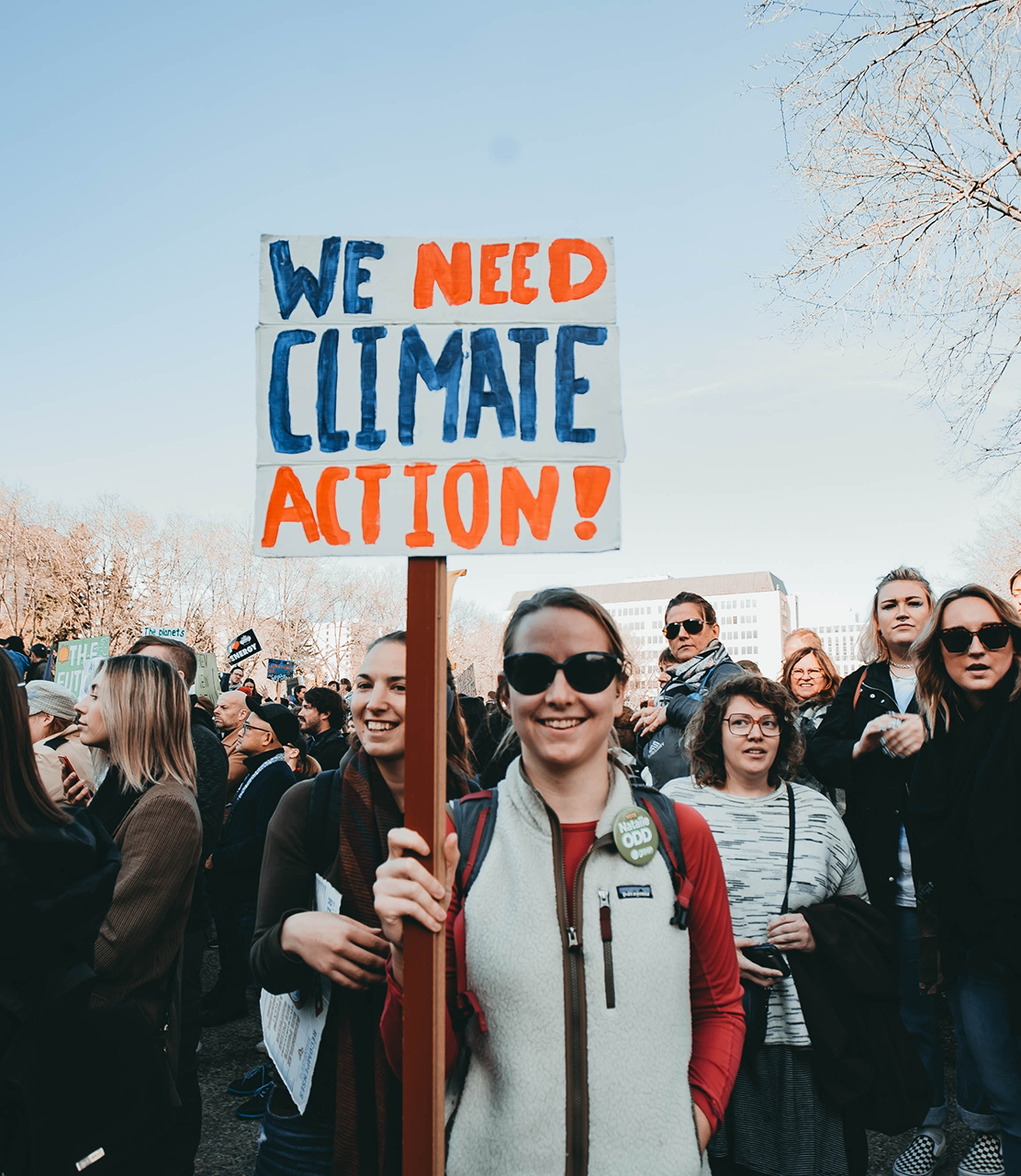 A person standing in front of group of protestors, holding a sign that says "We need climate action!"